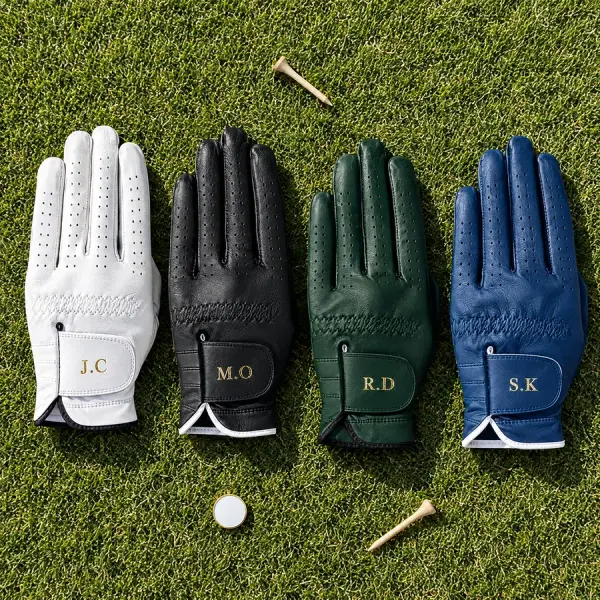Four gloves in white, black, green and navy with different initials laid on the grass